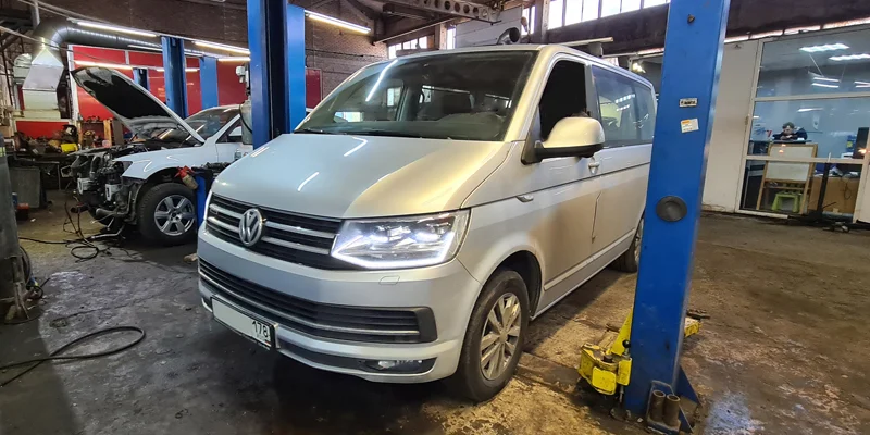 Серебристый Volkswagen Multivan T6 стоит в ремзоне у синего подъемника