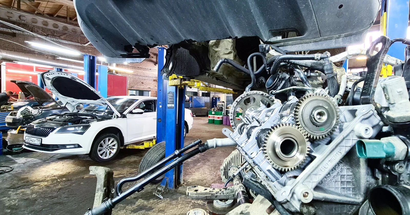 Снятый двигатель V6 под автомобилем на подъемнике, на фоне ремзона и Skoda Superb