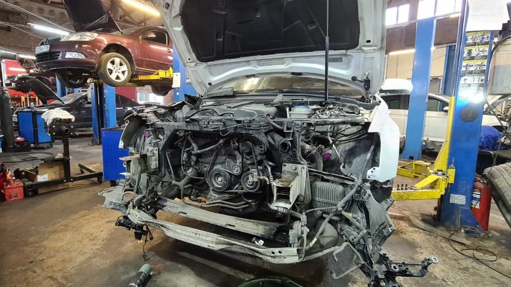 Автомобиль без бампера и радиаторов на посту автосервиса, на заднем плане подъемники